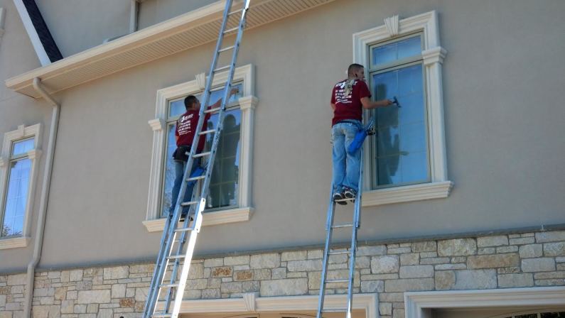 Two men on ladders cleaning the windows on a home